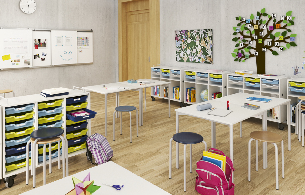 Ein Klassenzimmer mit Hockern und Tischen. Ein gebastelter Baum hängt an der Wand.